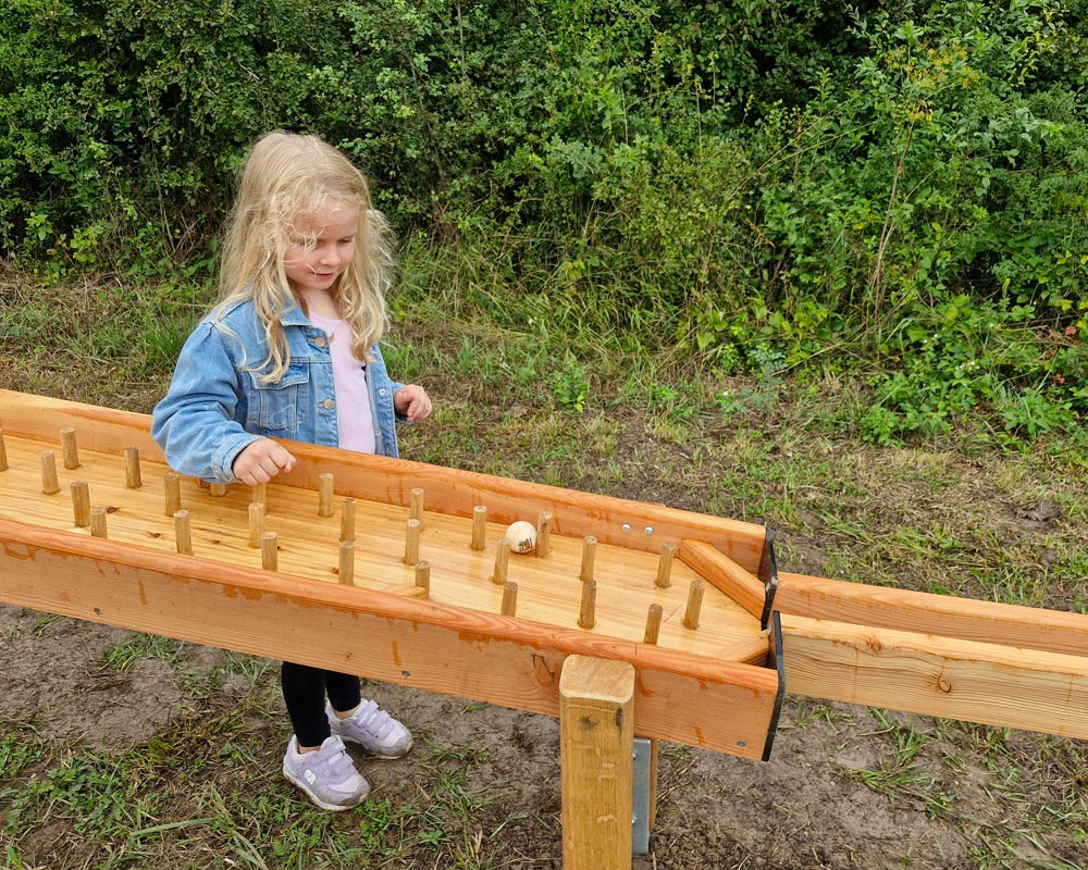 Kind verfolgt eine Holzkugel auf dem Weg über die Kugelbahn